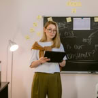 A young woman in business attire stands in an office holding a tablet, ready for a presentation.